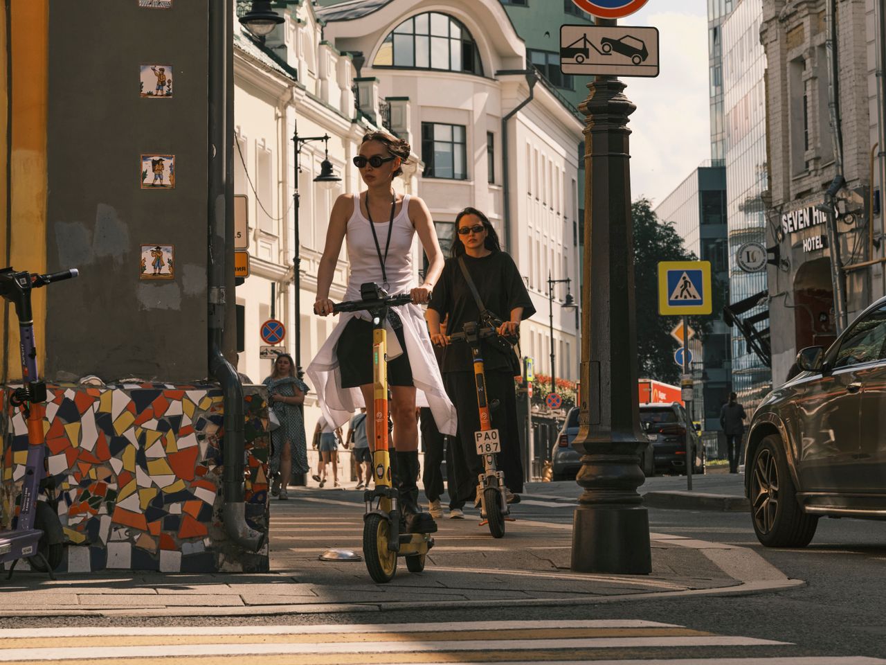 About Two women riding electric scooters on a city street, showcasing urban commute.
