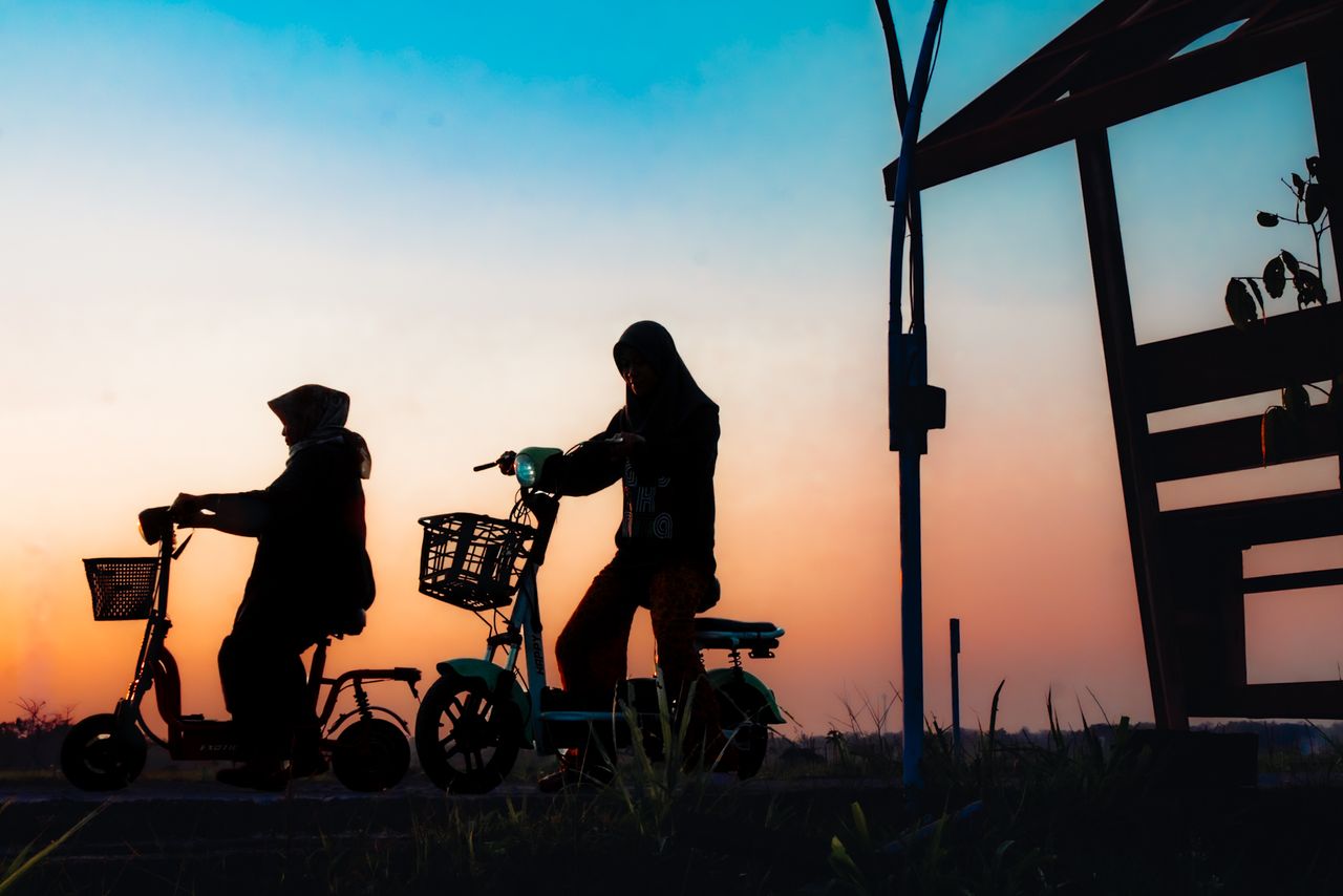 Services Two women on electric scooters silhouetted against a vibrant Jogja sunset.